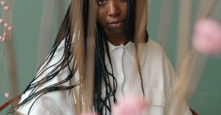 STEM Education - Self assured of young African American female millennial with long dark braids in stylish outfit sitting on chair and reading interesting illustrated book